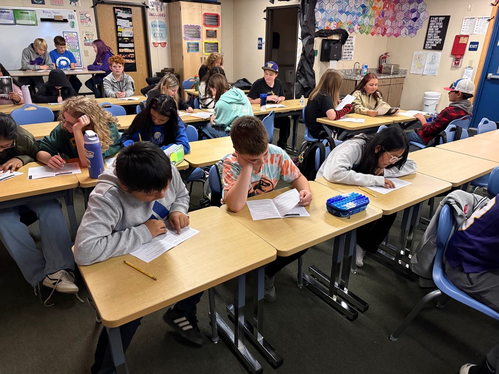 6th grade students work in small groups during a Halloween-themed classroom escape room challenge. Students are reading clues, solving puzzles, and discussing story elements together as part of a spooky ELA activity.