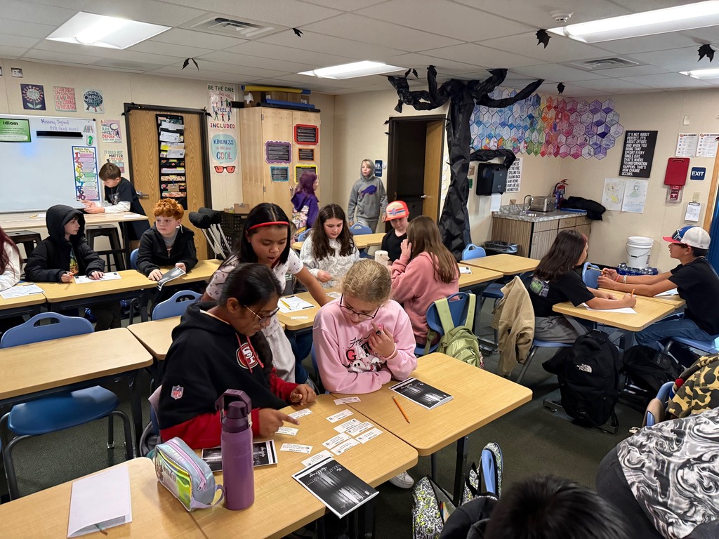 6th grade students work in small groups during a Halloween-themed classroom escape room challenge. Students are reading clues, solving puzzles, and discussing story elements together as part of a spooky ELA activity.