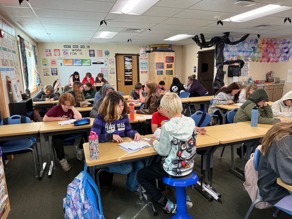 6th grade students work in small groups during a Halloween-themed classroom escape room challenge. Students are reading clues, solving puzzles, and discussing story elements together as part of a spooky ELA activity.