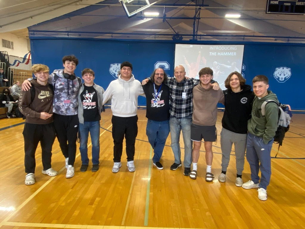 Matt Hamill smiles alongside Sedro-Woolley High School students during a previous visit to the school, standing in the gym surrounded by excited students and staff.