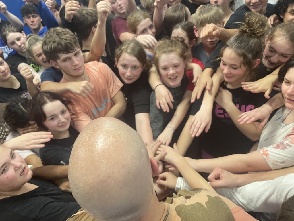 Matt Hamill smiles alongside Sedro-Woolley High School students during a previous visit to the school, standing in the gym surrounded by excited students and staff.