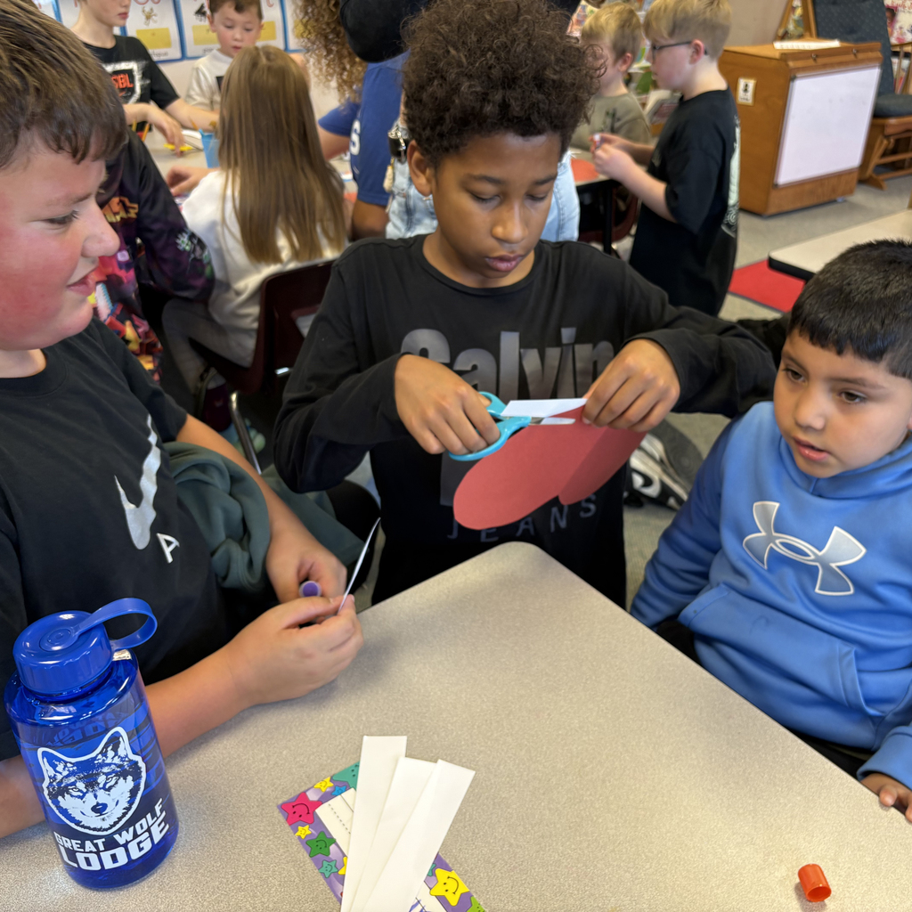 Kindergarten and sixth grade students work together to cut and glue red, white, and blue paper hearts and stars for Veterans Day decorations.