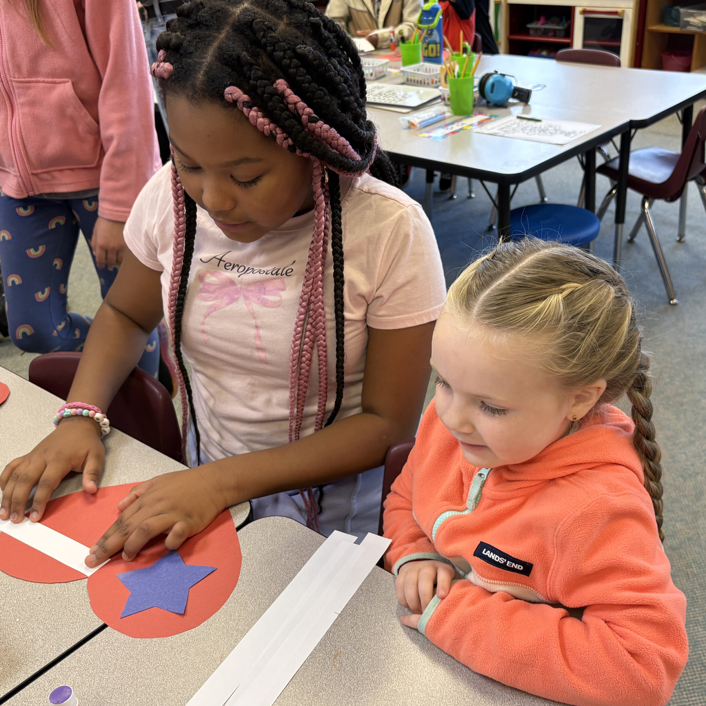 Kindergarten and sixth grade students work together to cut and glue red, white, and blue paper hearts and stars for Veterans Day decorations.