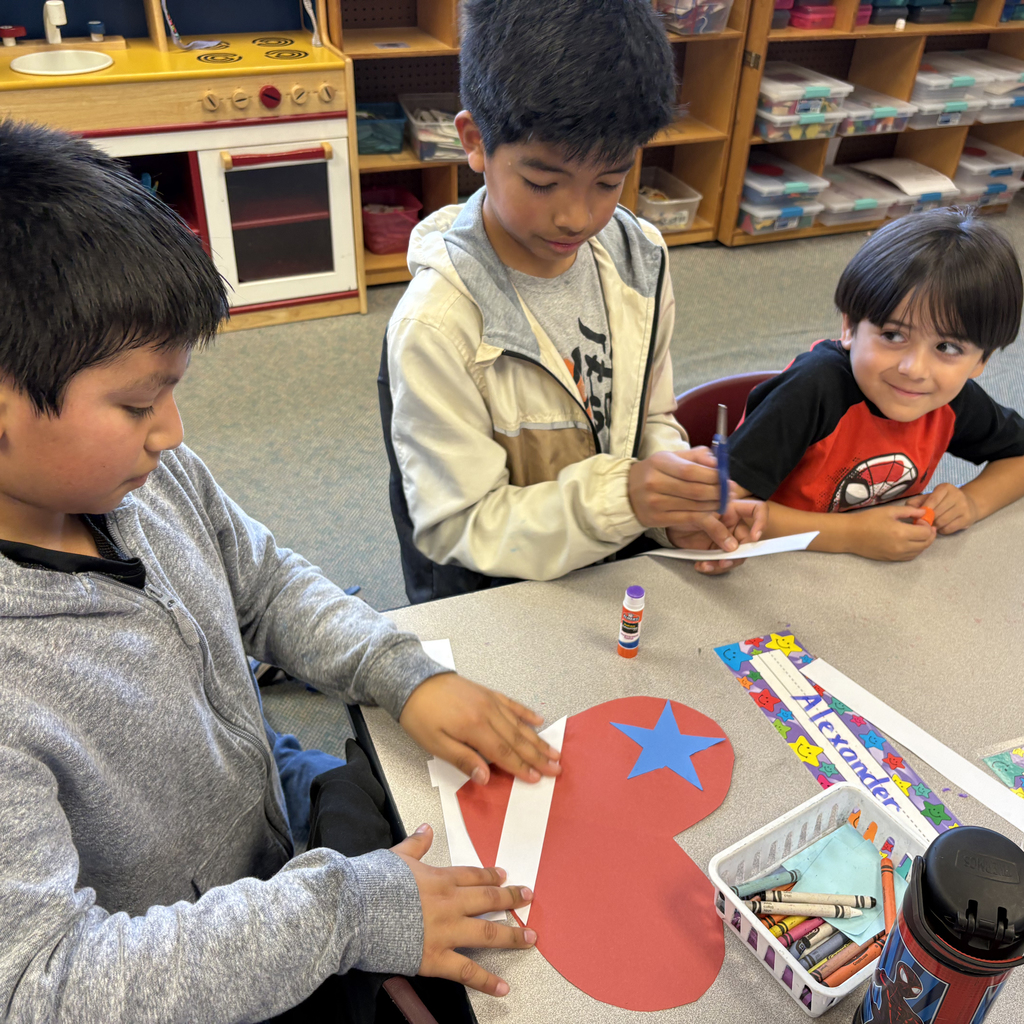 Kindergarten and sixth grade students work together to cut and glue red, white, and blue paper hearts and stars for Veterans Day decorations.