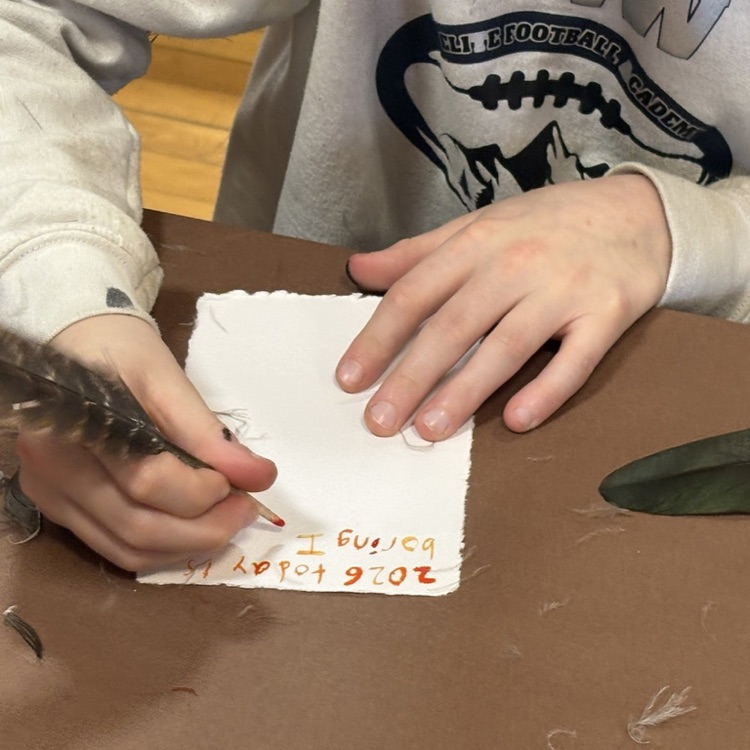 Close-up of a student writing with a feather quill dipped in ink.