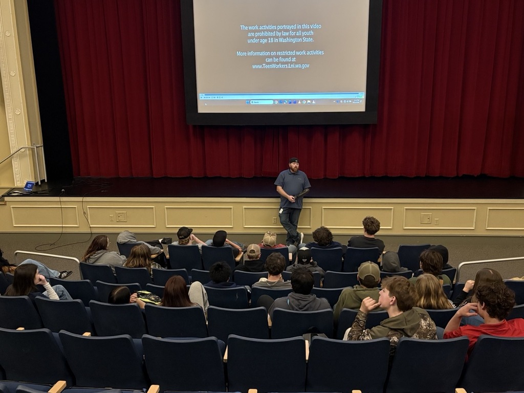 Matt Pomerinke presents to a seated audience of high school students in an auditorium, discussing the importance of safety training and awareness for young workers.
