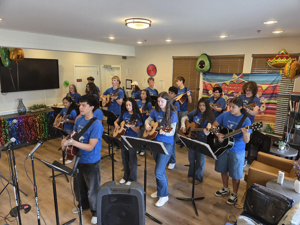 A group of Sedro-Woolley High School mariachi students perform with instruments for residents gathered indoors, many seated and watching with smiles during a Cinco de Mayo celebration.