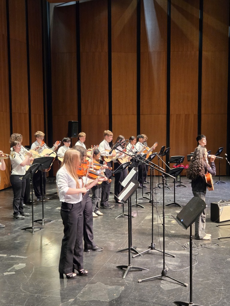 Students from several local schools perform mariachi music and folklórico dance on stage at McIntyre Hall during a regional Mariachi Festival. Photos show student musicians in traditional mariachi attire performing with instruments and large combined group performances celebrating music and culture.