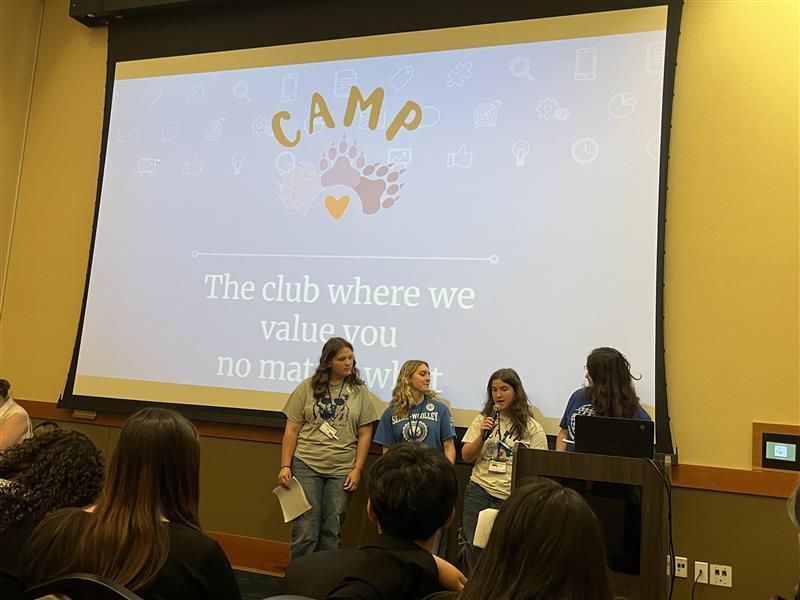 Four Sedro-Woolley High School students stand beside a presentation display at the Spring Youth Forum at Great Wolf Lodge. The students represented the SWHS CAMP Club (Cubs Advocating for Mental Health and Prevention), sharing projects that promote kindness, inclusion, mental health awareness and school connectedness. The display includes photos and examples of student-led activities designed to help classmates feel welcomed, valued and supported.