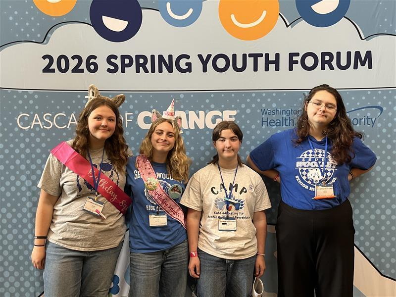 Four Sedro-Woolley High School students stand beside a presentation display at the Spring Youth Forum at Great Wolf Lodge. The students represented the SWHS CAMP Club (Cubs Advocating for Mental Health and Prevention), sharing projects that promote kindness, inclusion, mental health awareness and school connectedness. The display includes photos and examples of student-led activities designed to help classmates feel welcomed, valued and supported.
