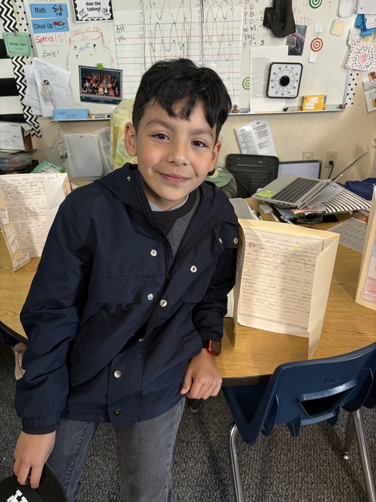 Third grade students at Evergreen STEM Elementary stand beside biography displays and presentation boards, sharing research projects about notable historical and contemporary figures with visitors during the school’s first Biography-palooza event.