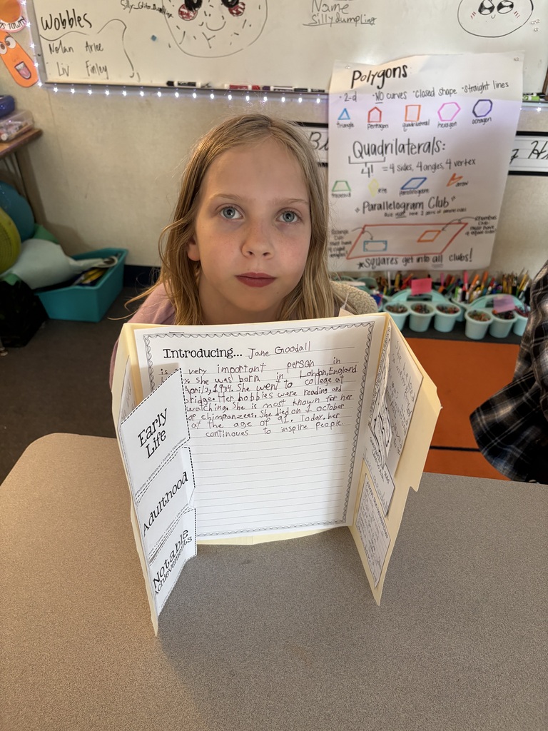 Third grade students at Evergreen STEM Elementary stand beside biography displays and presentation boards, sharing research projects about notable historical and contemporary figures with visitors during the school’s first Biography-palooza event.