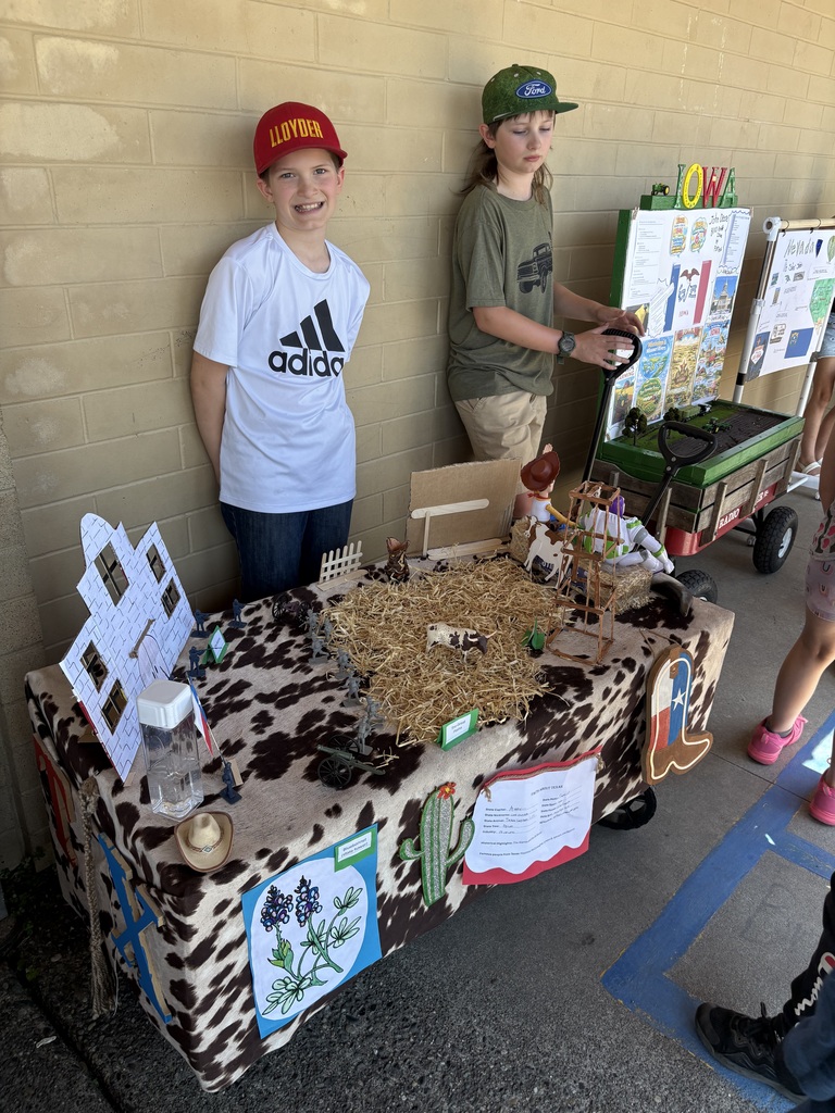 Evergreen STEM Elementary fourth grade students stand beside colorful state-themed floats they created for the annual Float Parade. The projects feature maps, landmarks, state symbols, and other research-based displays as students share information about their assigned states with visitors.