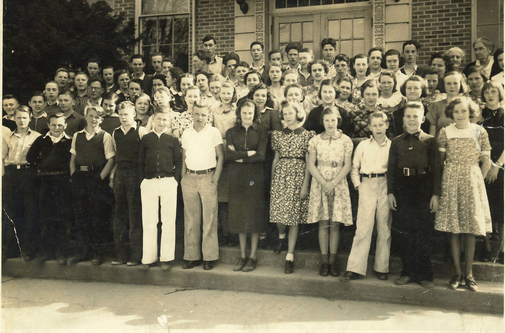 1938 class photo: Black-and-white historic photograph believed to show Central School's seventh- and eighth-grade students in 1938. A large group of students and adults pose in several rows on the steps outside the brick Central School building.
