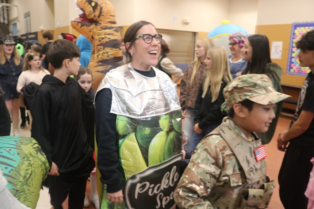 Evergreen Elementary School students dressed in Halloween costumes parade through the hallways of Cascade Middle School. Middle school students, many also in costume, line the hallways to exchange high fives and fist bumps with younger students. Other photos capture happy reunions between former Evergreen students and staff members.