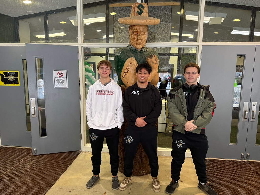 State wrestlers standing behind wood Ranger statue
