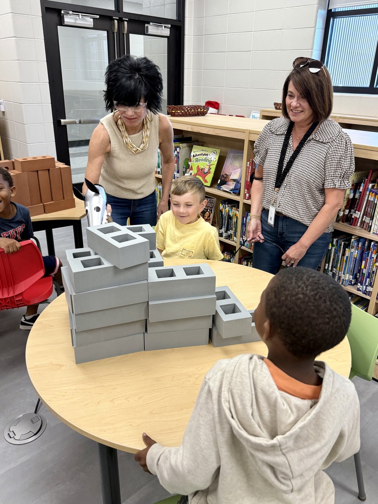 Miss Jodi Harper and Miss Jalee’ Conley’s class had an enrichment activity in the library. Mrs. Godwin read, “No Lie, Pigs (And Their Houses) Can Fly!” and a non fiction book about pigs. Students had to identify the characters and the setting of the story and the difference between fiction and non fiction texts. After the story, students had to create their own houses (setting) around a pig (character) taped to the tables. Items to build the houses included magnatiles, magnetic blocks, cups, dominoes, lincoln logs, fake bricks, and fake cement blocks. The idea was to make it strong enough not to get blown down. Miss Jodi used a hair dryer as the Big Bad Wolf. The class had lots of fun with this activity. 