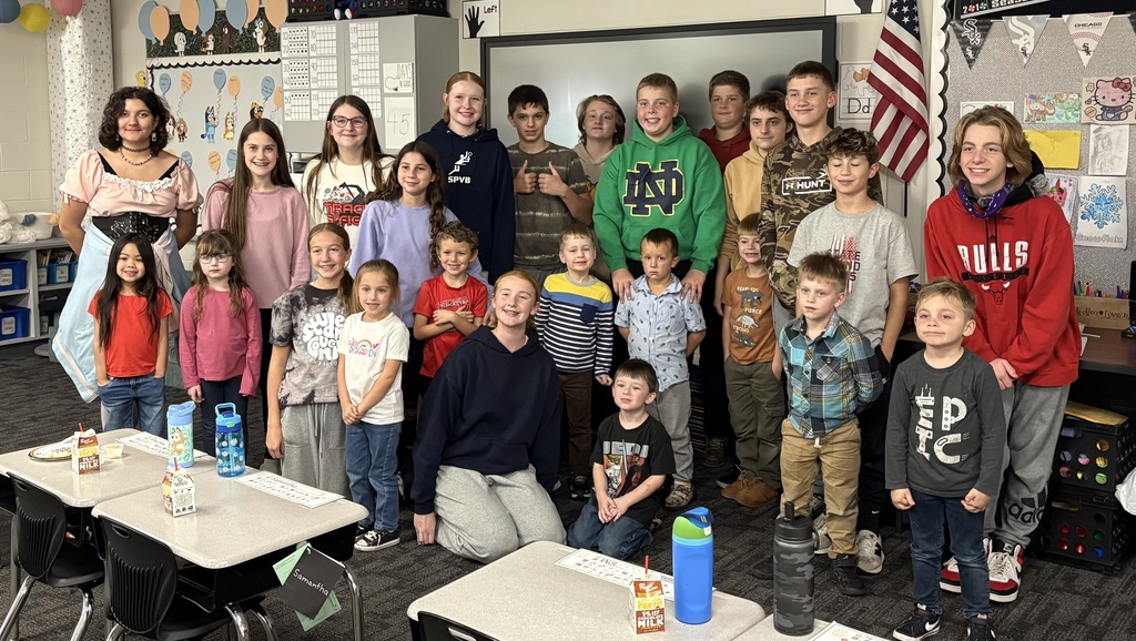 A group of eighth grade and kindergarten buddies stand together smiling.  
