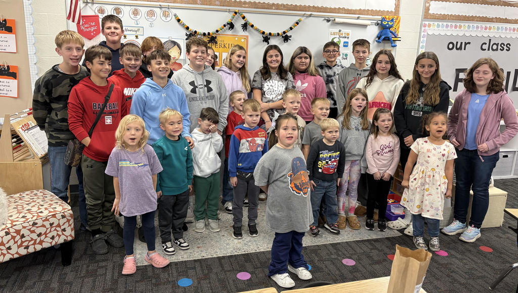 A group of eighth grade and kindergarten buddies stand together smiling.  