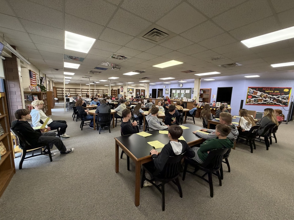 Students sit around tables in a library discussing the Holocaust with a teacher.  