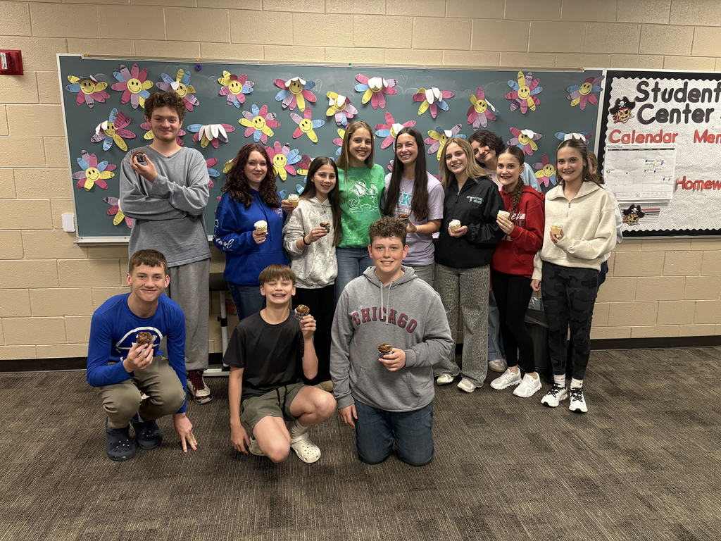 Middle school students pose with cupcakes and their student teacher.  
