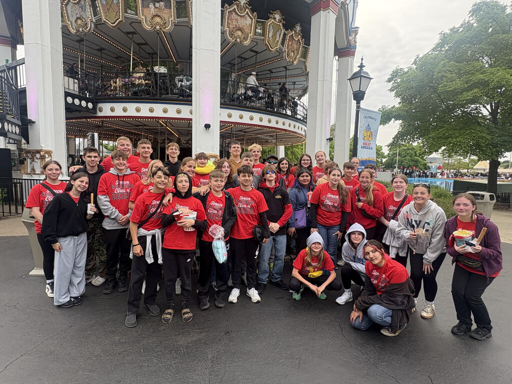 Students pose in matching shirts at an amusement park.  