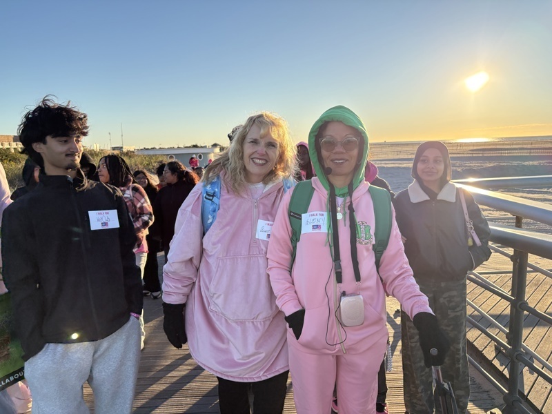 A group of people walks on a wooden boardwalk during the day, wearing jackets.