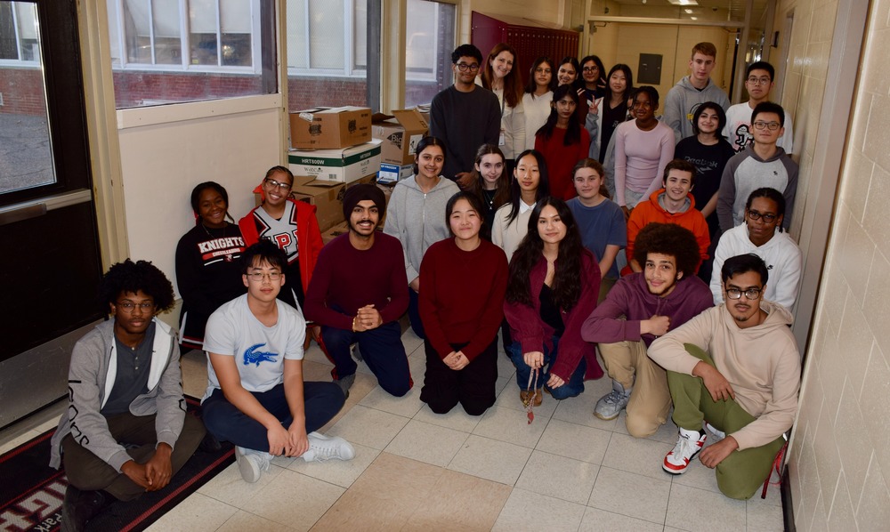  group of young adults pose together in a school hallway, smiling.