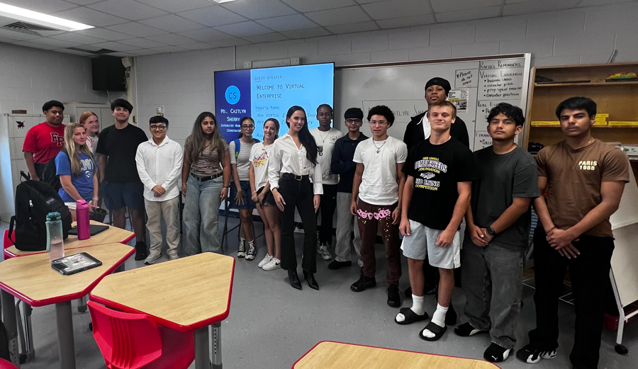 Large group of students smiling together in classroom with alumni.