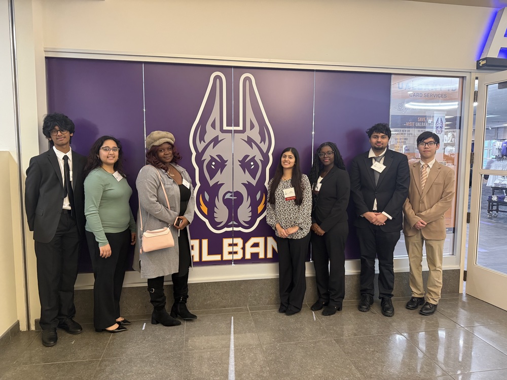 Students standing in front of UAlbany logo.
