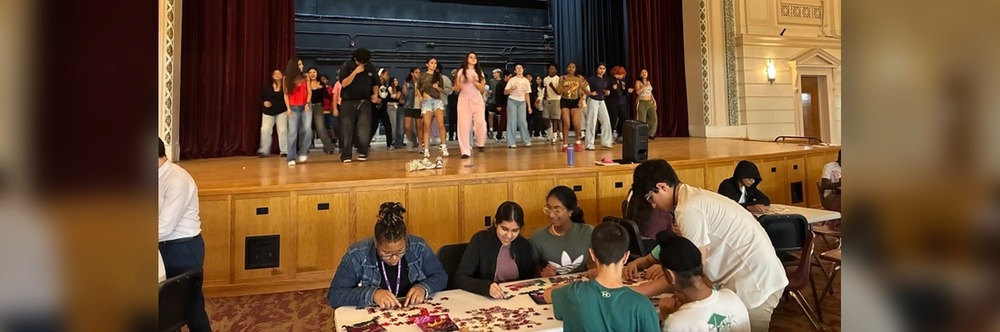 A group performs on stage while others engage in activities at tables below.