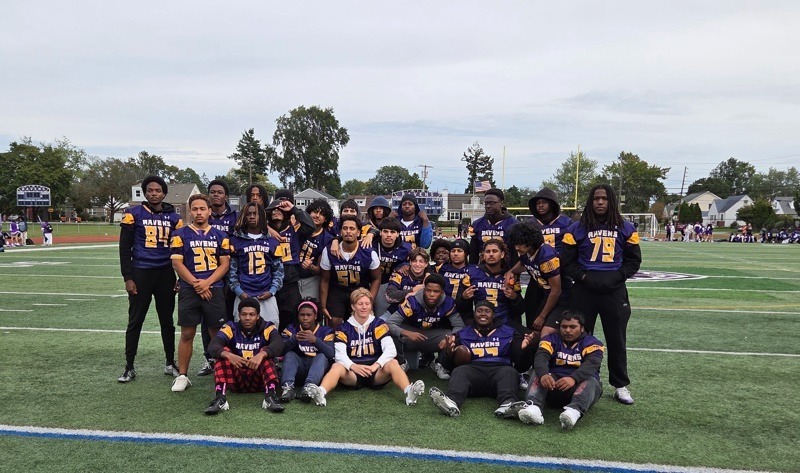 A group poses together on a football field, wearing team jerseys and athletic clothing.