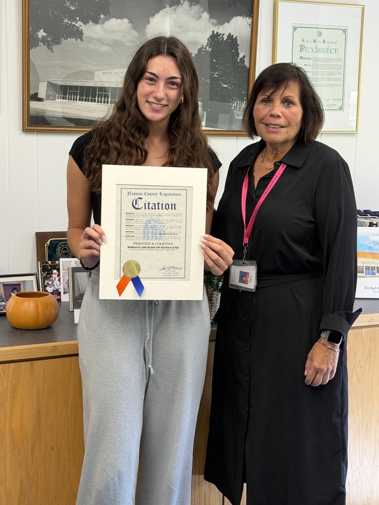 Student holding certificate, standing with teacher.