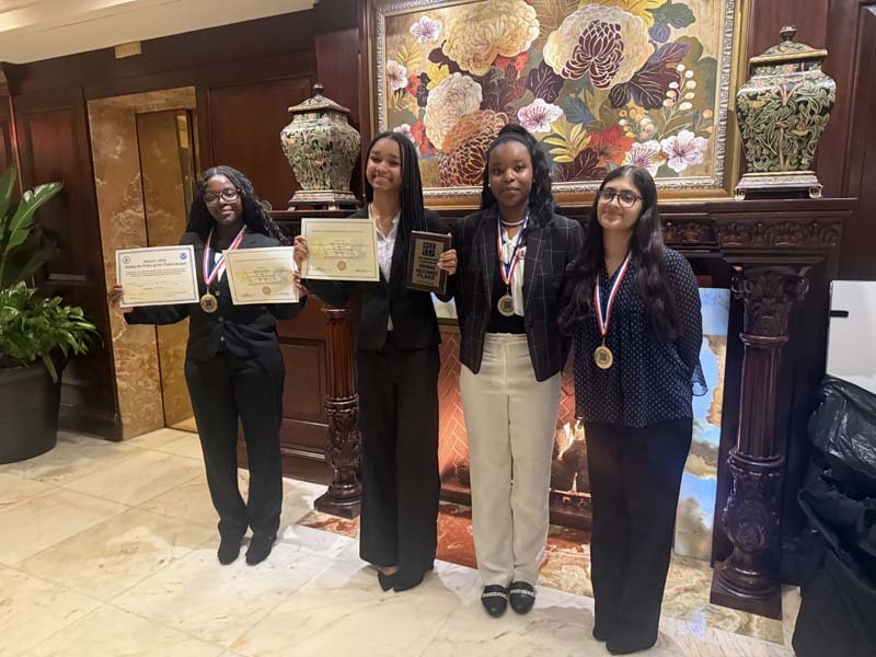 Students holding certificates in front of fireplace with painting.