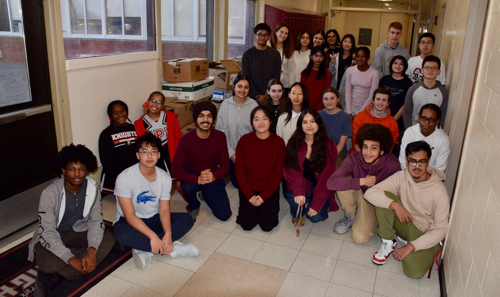  group of young adults pose together in a school hallway, smiling.