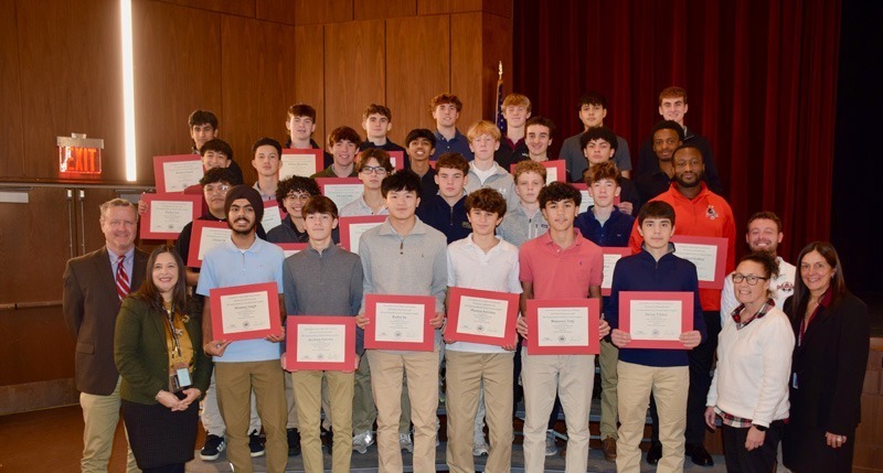 A group of students holding certificates stands on a stage with teachers.