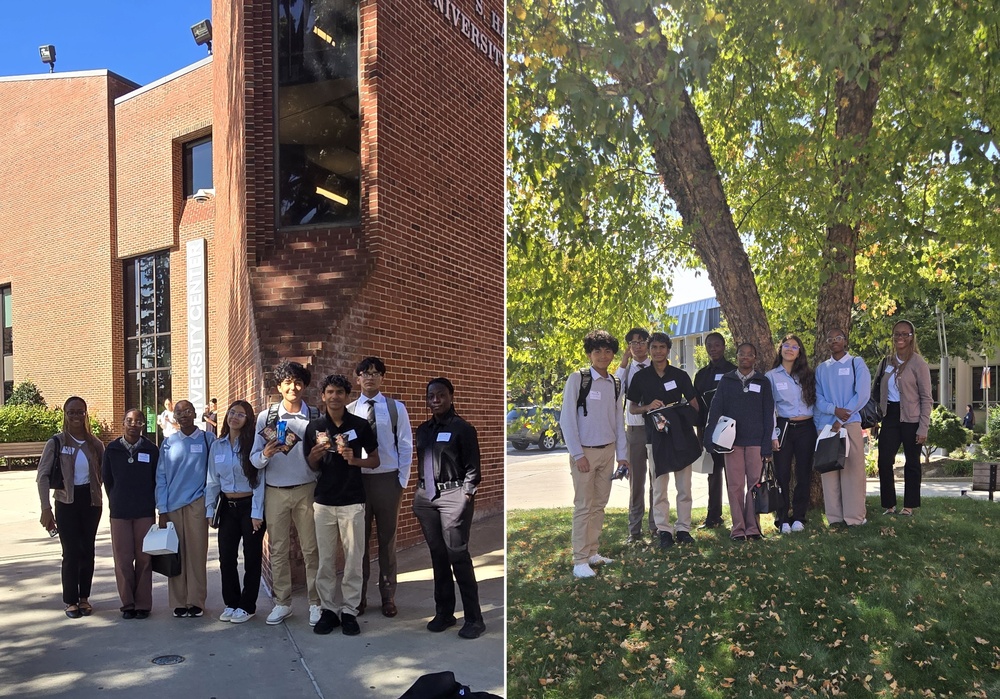 A group stands outside a university building, posing for a photo under a tree.