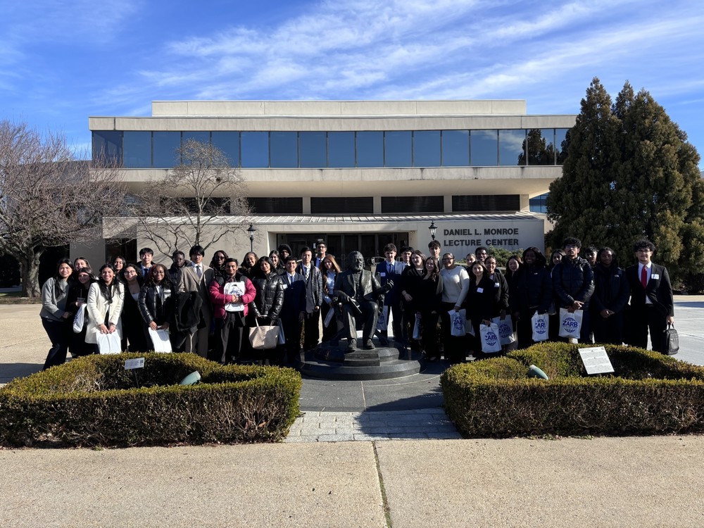 A group of smiling people stands in front of the Daniel L. Monroe Lecture Center