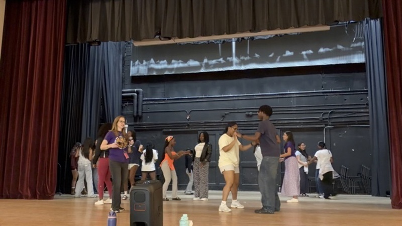 A group performs on stage while others engage in activities at tables below.