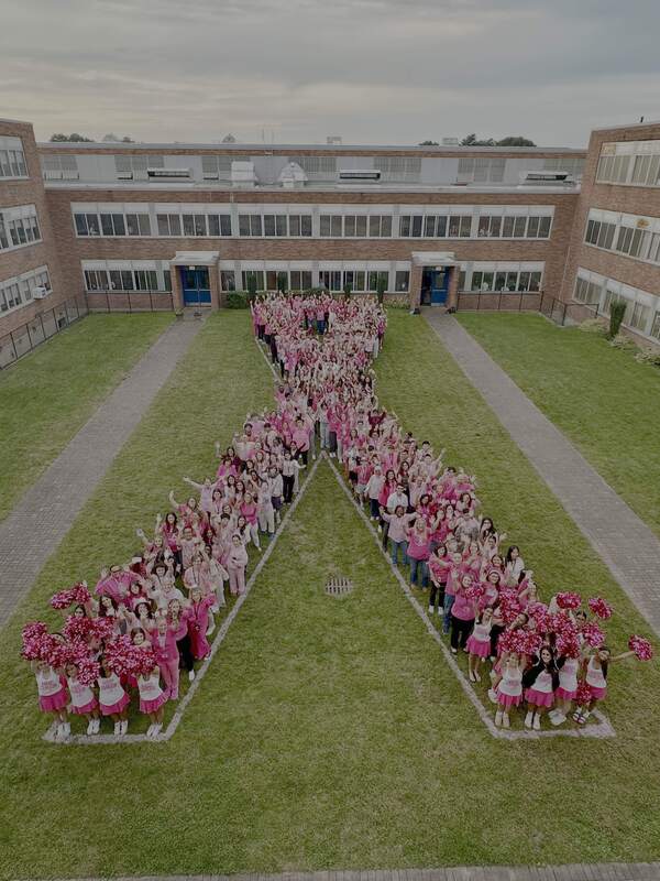students and staff dressed in pink and gathered outside before the start of the school day to form a pink ribbon