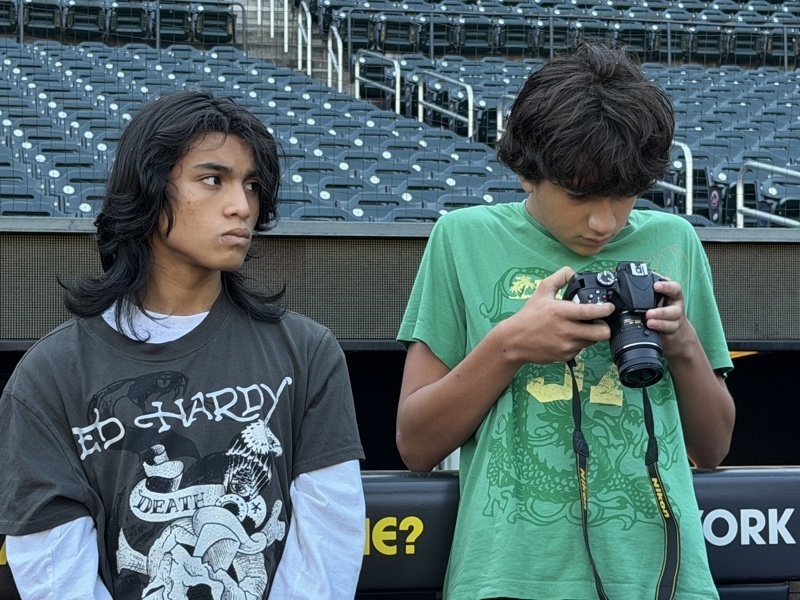 Two people stand at a stadium, one holding a camera and the other observing.