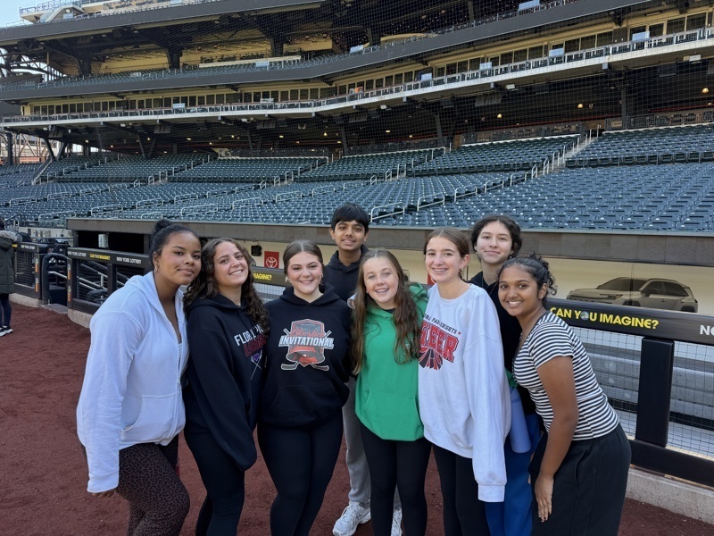 A group poses together at a sports venue, holding a plaque.