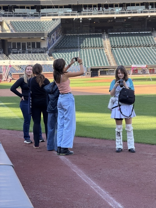 A group of people stands on a baseball field, with two individuals taking photos.