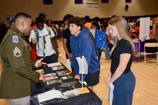 Students listening to older person talk at table.