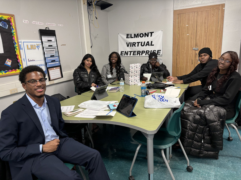 people sit at a table, smiling and writing on paper near a tablet. 