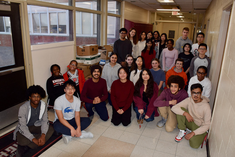  group of young adults pose together in a school hallway, smiling.