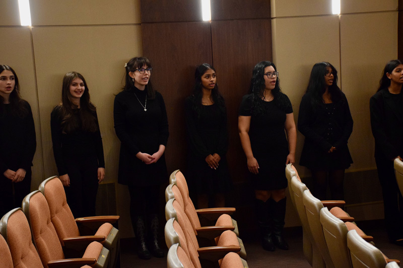 A group of young adults, stand in a theater's side seating area