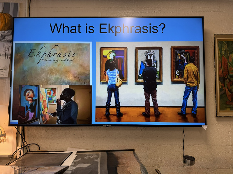 A classroom filled with students sitting at wooden tables, attentively facing forward. The room is decorated with art and plants, creating a lively atmosphere.