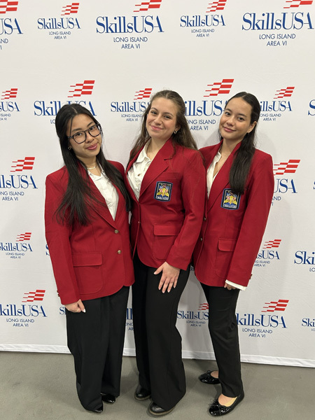 Three young women in red blazers with patches stand smiling in front of a SkillsUSA Long Island Area VI backdrop, exuding pride and confidence.