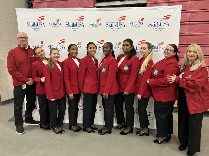 Three young women in red blazers with patches stand smiling in front of a SkillsUSA Long Island Area VI backdrop, exuding pride and confidence.